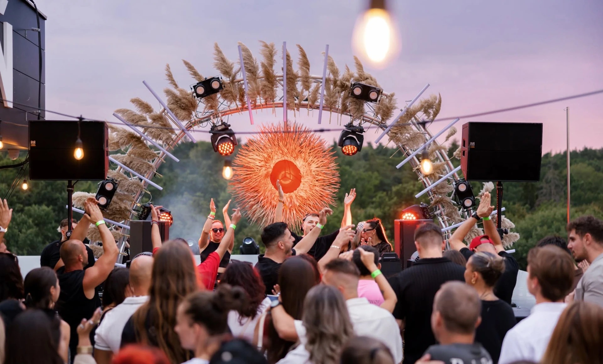 Večerná stage dekorácia: oblúková konštrukcia s pampasovou trávou a svietiacou guľou nad DJ pultom