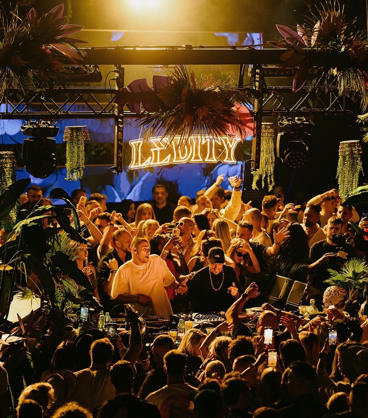 Festival Levity: DJ pult pod zlatým neónovým nápisom a palmami nad davom