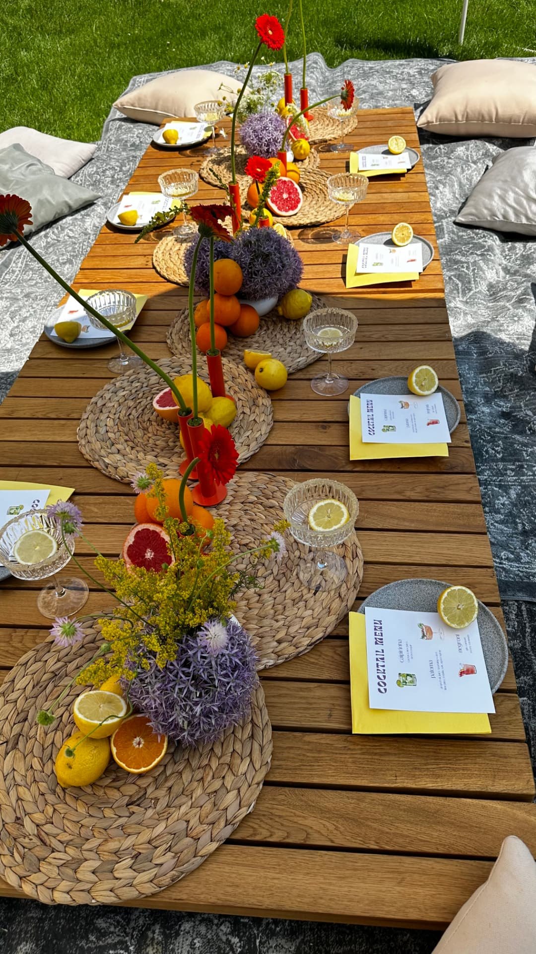 Private Moments — Baske Vila: piknikový stôl pri zemi s citrusmi, koktailovými pohármi, menu a vysokými vázičkami s alliom a gerberami